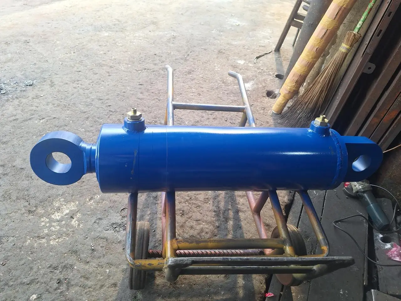 Custom blue hydraulic cylinder with clevis eyes on a workshop trolley, side view